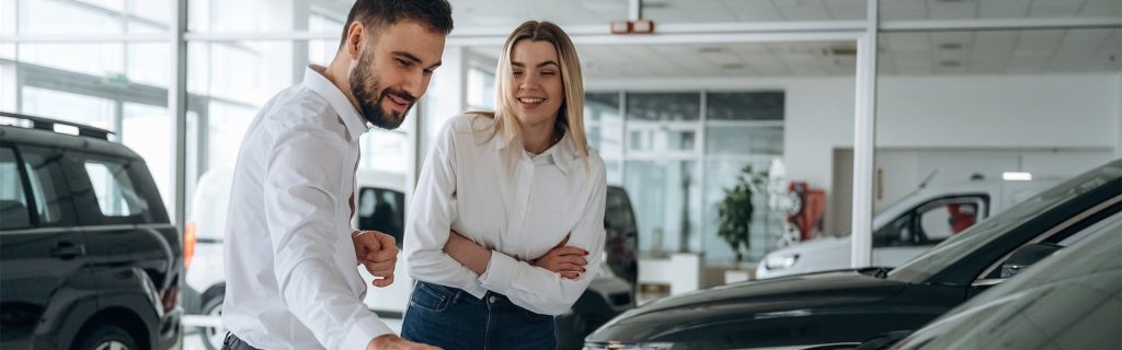 A couple wearing matching white shirts are walking through a GMC SUV showroom checking out the vehicles with smiles on their faces